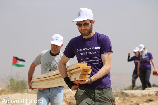 פעיל פלסטיני ופעיל יהודי אמריקאי נושאים ביחד קורות עץ כדי לבנות את אחד מאוהלי המאחז. "צומוד, מחנה החירות". הכפר סארורה הגדה המערבית, 19 במאי 2017 (צילום: אחמד אל-באז אקטיבסטילס)