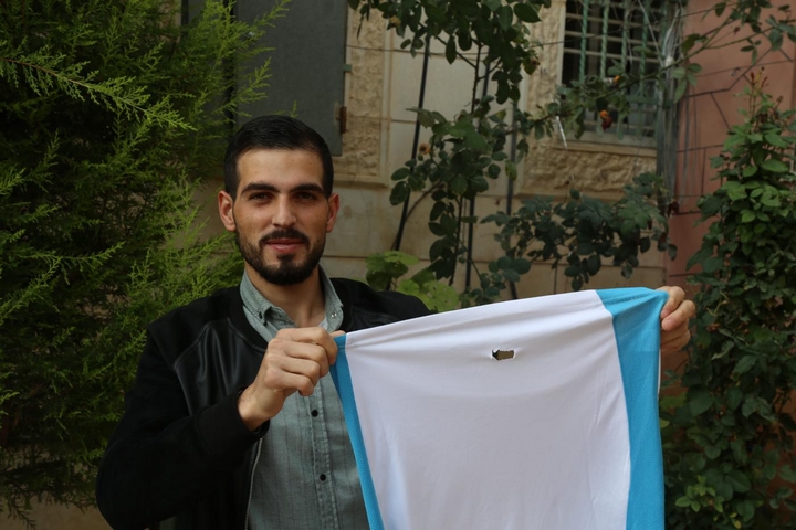 כראם קאוואסמי, פלסטיני בן 22 מחברון, מחזיק את החולצה שלבש כשחייל ישראלי ירה בו בגבו בכדור ספוג (צילום: MEE/Alaa Daraghmeh)
