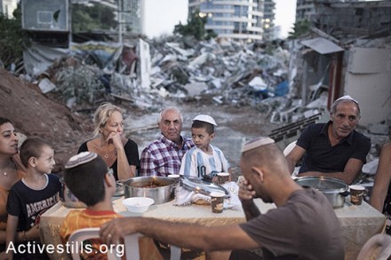 משפחת חליף יושבת לשולחן שבת ומאחוריהם חורבות ביתם שנהרס על ידי חברות פרטיות לאחר פינויים, גבעת עמל, ה-19 בספטמבר, 2014. (שירז גרינבאום/אקטיבסטילס)