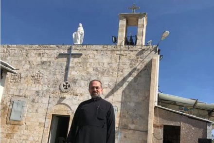 התחילו עם הלוויות בבית הקברות של הכפר ההרוס, עכשיו עברו לחתונות. כוהן הדת סוהיל ח'ורי על רקע הכנסייה באיקרית (צילום באדיבות דף הפייסבוק איקרית)